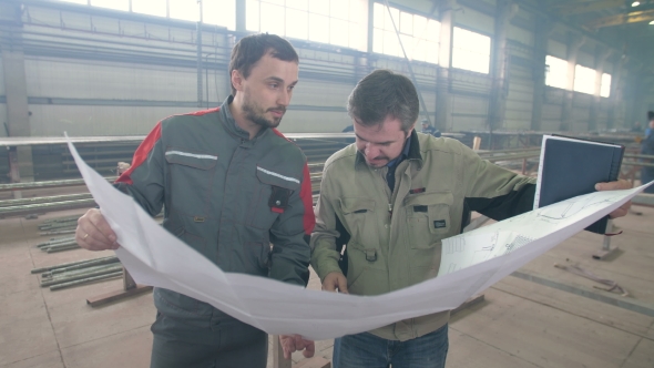 Two Workers Look at the Drawing at the Factory