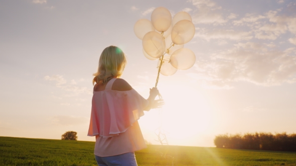 Carefree Young Woman with Balloons Walking on a Green Meadow at Sunset. Concept