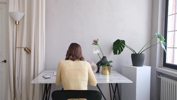 Woman in Polo Shirt at Table with Lush Houseplants in Room