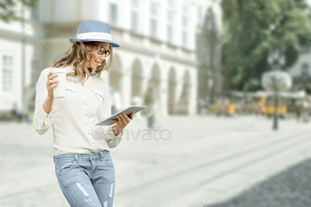 , holding tablet in her hands, reading news and studying against urban city background.