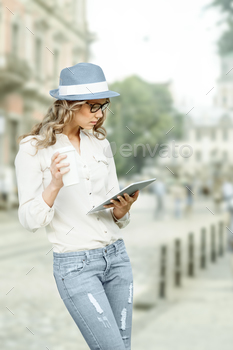 , holding tablet in her hands, reading news and studying against urban city background.