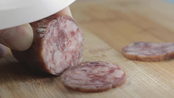 Sausage Sliced on a Wooden Board with a White Ceramic Knife
