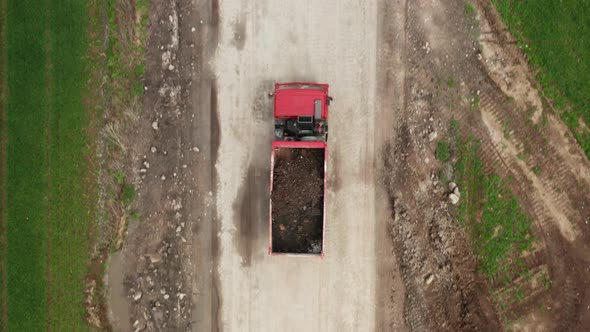 Red Lorry Carrying Soil From the Field Along a Dirt Road Between Two Green Fields