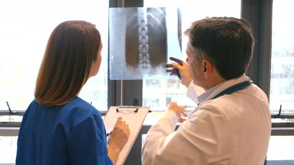 Doctor examining x-ray while nurse writing on clipboard