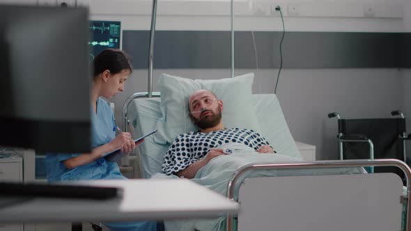 Sick Man Sitting in Bed with Oxygen Tube Explaining Sickness Symptom to Medical Nurse