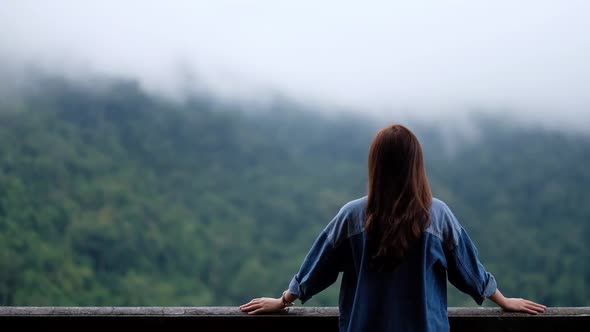 Rear view of a female traveler looking at a beautiful green mountain on foggy day