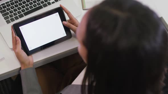 Biracial businesswoman sitting at desk, using tablet with copy space in modern office