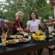Man Passing Food To People Sitting At Table Eating Young Friends Group Gathering On Summer Terrace - VideoHive Item for Sale
