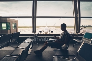 . Young man using mobile phone and waiting for his flight.