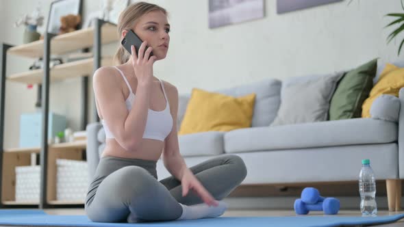 Young Woman Talking on Smartphone on Yoga Mat at Home