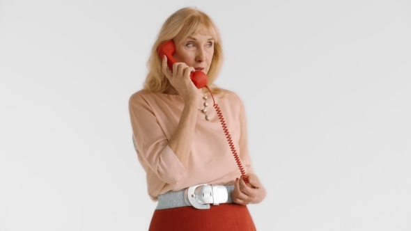 Beautiful Elegant Elderly Blond Woman Uses Red Landline Phone Handset and Talks with Her Friend