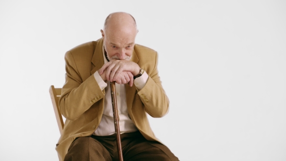 Sad Lonely Old Man with Piercing Eyes Sitting in Armchair with Hands and Head on His Cane