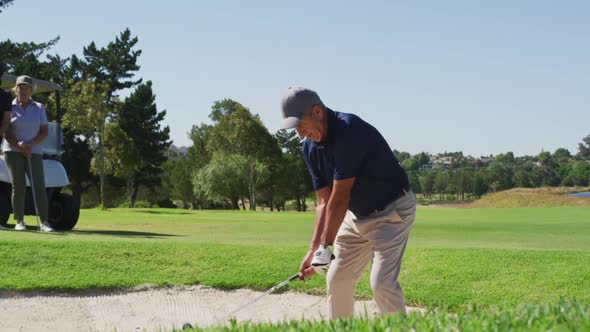 Caucasian senior man hitting golf ball out of a sand trap at golf course on a bright sunny day