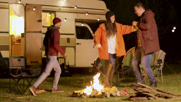 Group of Close Friends Dancing Around Camp Fire in a Cold Night of Autumn