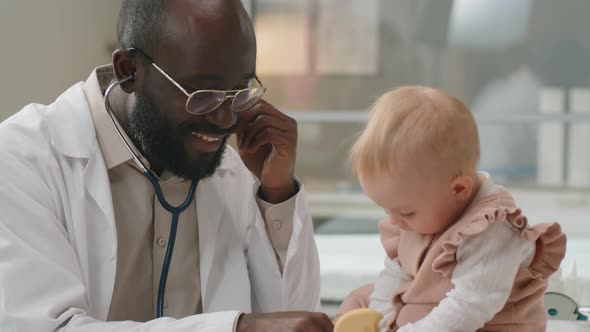 Black Pediatrician Using Stethoscope and Giving Checkup to Caucasian Baby