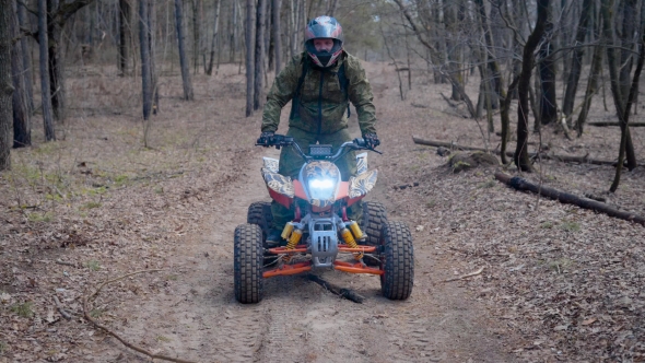 Man in Protective Equipment and Helmet Operating ATV Moving Along the Road in the Forest Gliding