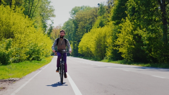 A Bearded Man with a Backpack Rides a Bicycle Along a Bicycle Path