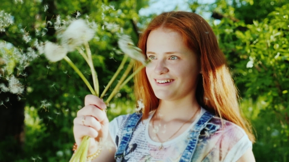 A Girl with Bright Red Hair Has Fun, Plays with Dandelion Flowers