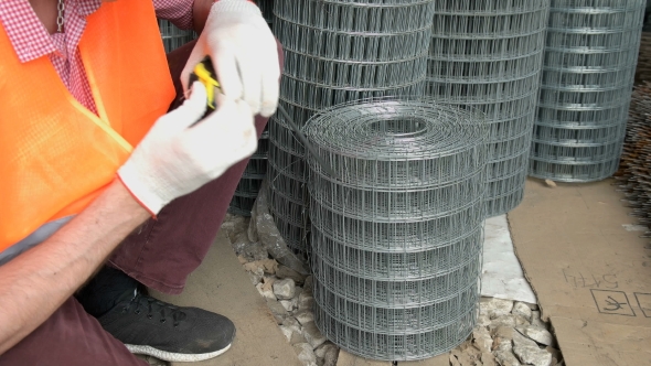 The Worker Measures with a Tape Measure the Width of the Iron Grid