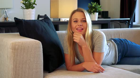 Young Woman Lies on a Couch in a Living Room and Smiles To Camera