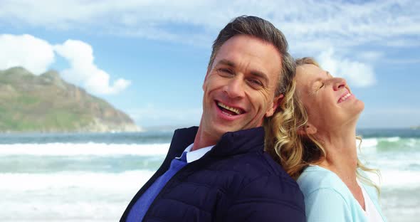 Mature couple standing back to back on beach