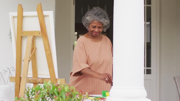 Senior african american woman painting while standing on the porch of the house