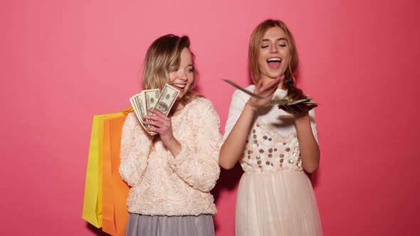 Two young stylish smiling blond women holding shopping bags and making rain money