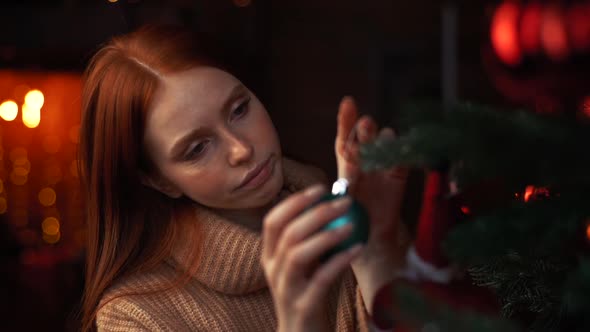 Close-up Face of Sad Redhead Young Woman Decorating Christmas Tree Alone at Cozy Living Room