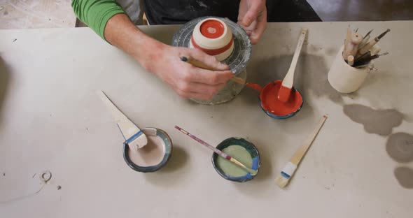 Overhead view of male potter using brush to paint pot on potters wheel at pottery studio