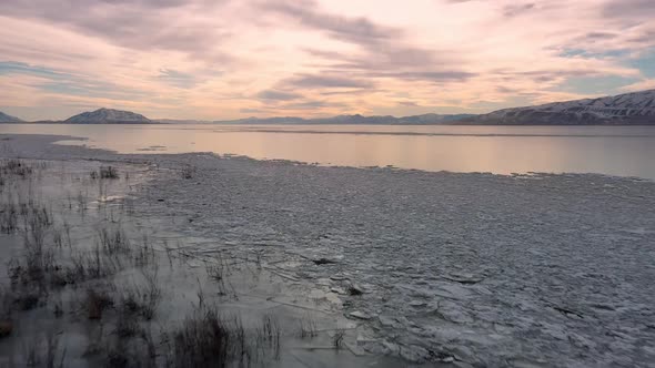 Flying over shoreline ofr frozen lake towards sunset