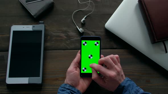 Hands of Man Using Smartphone  with Green Screen on Wood Table