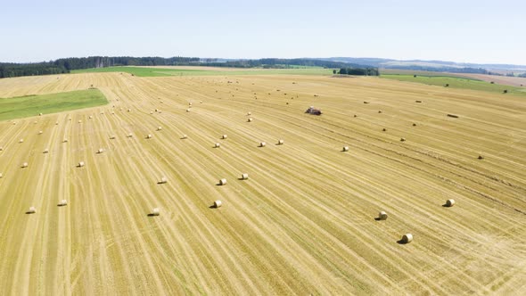 Aerial Drone Shot  a Field with a Tractor and Hay Bales in a Rural Area on a Sunny Day