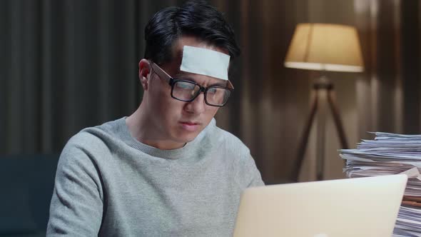 Close Up Of Sick Asian Man Typing Laptop Computer While Working Hard With Documents At Home