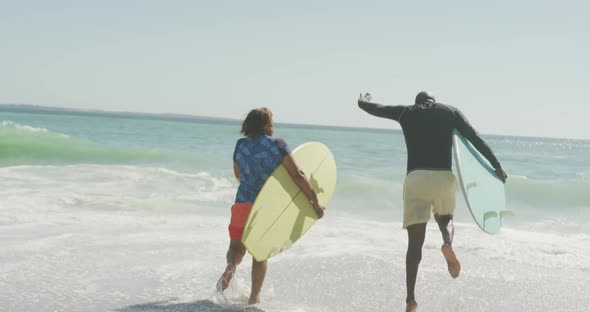 Senior african american couple running with surfboard on sunny beach