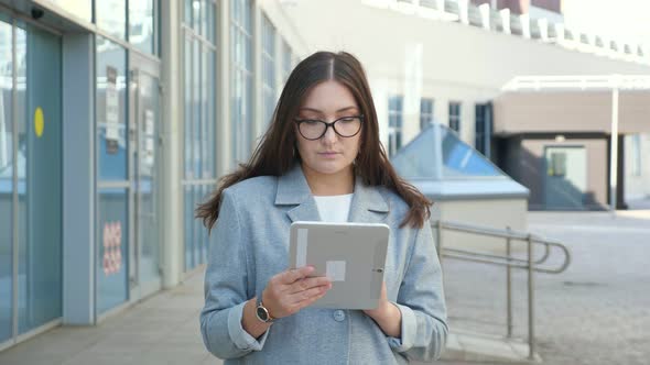 Young Woman in a Formal Suit and Glasses Looks Into a Tablet on the Street Slow Motion