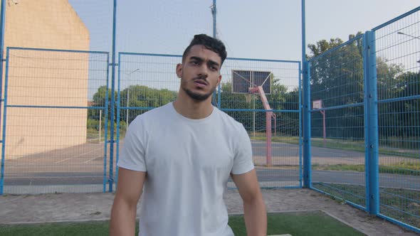 Tired Young Middle Eastern Arabic Athlete in Summer Sportswear Walking Moving Along Stadium Fence