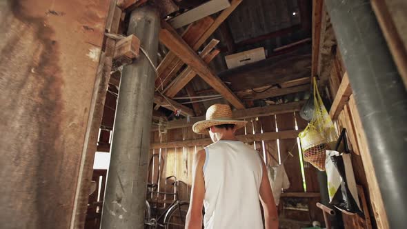 A Country Boy Wearing a Straw Hat Walking Through Bright Light Into a Shed To Get His Bicycle Slow