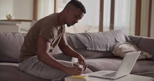Black Man Writing Down Data From Laptop