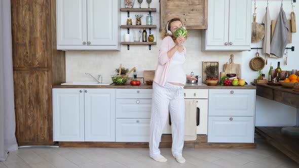 Young Pregnant Woman Singing In Broccoli Wearing Headphones Dancing In Kitchen