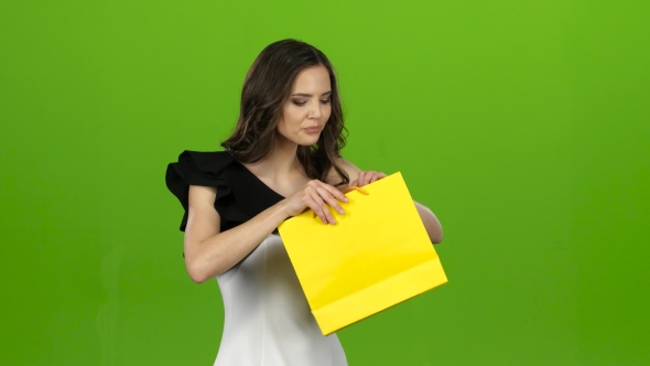 Brunette Girl Holds a Gift Bag in Her Hands, She Likes It. Green Screen