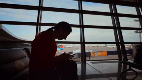 Businesswoman at Airport with Phone in Hands Against the Large Panoramic Window with Parking