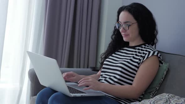 Woman Typing on Laptop Sitting on Sofa at Home, Businesswoman Sits at Home Types on Smartphone