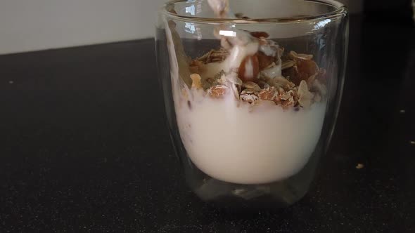 Mixing Yogurt with Muesli and Raisins with a Metal spoon in a Class cup (Slowmotion)
