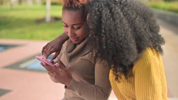 Two young black african women chatting and watching photos in the phone