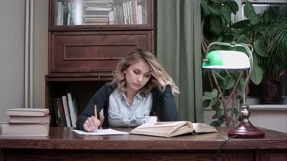 Young Woman Sitting at Desk Tired of Working and Taking Her Head in Hands