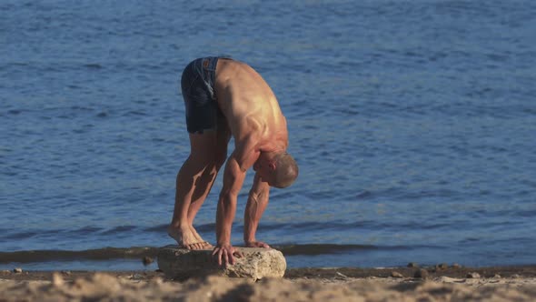 Sports Exercises Outdoors  Young Fit Man Starts to Stand on His Hands on the Stone on a Beach