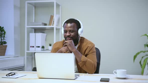 African is Chatting Online Through Headphones in Computer on Table in Room Spbas