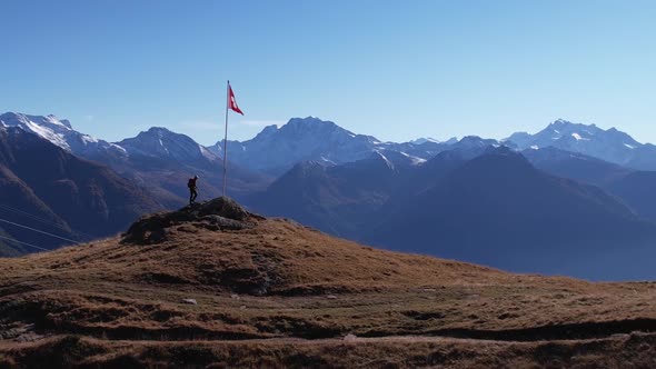 Solo male hiker climbs mountain summit with waving swiss flag and epic outlook