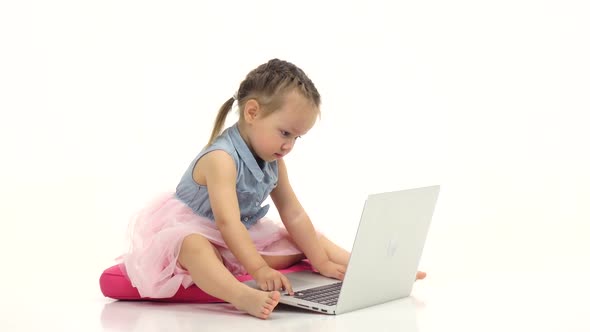 Little Girl Is Sitting on Her Lap and Looking at the Laptop. White Background