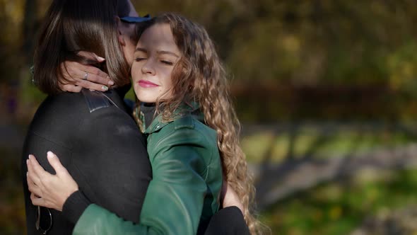 a Blonde in a Green Jacket Hugs a Man in Sunglasses in an Autumn Park on a Sunny Day